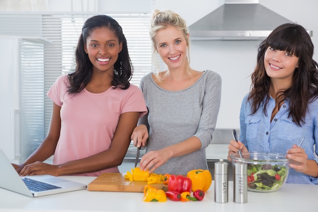 Nette Freunde, die Salat machen und Laptop für das Rezept betrachten Kamera verwenden