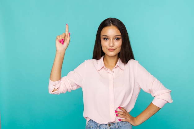 Nette glückliche Frau in der weißen Bluse, die etwas durch ihren Finger zeigt.