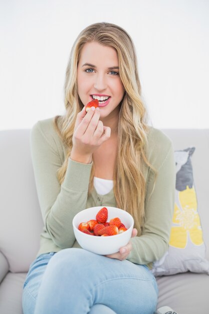 Nette hübsche Blondine, welche die Erdbeeren sitzen auf gemütlichem Sofa isst