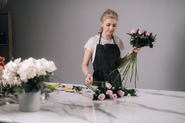 Nette junge Floristin mit Schürze, die Blumenarrangement macht