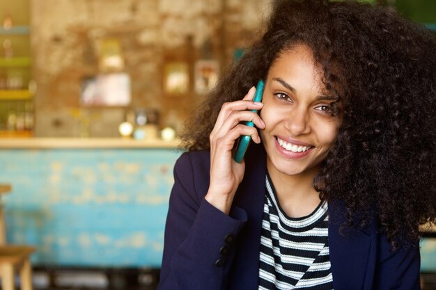 Nette junge Frau, die am Handy am Café spricht