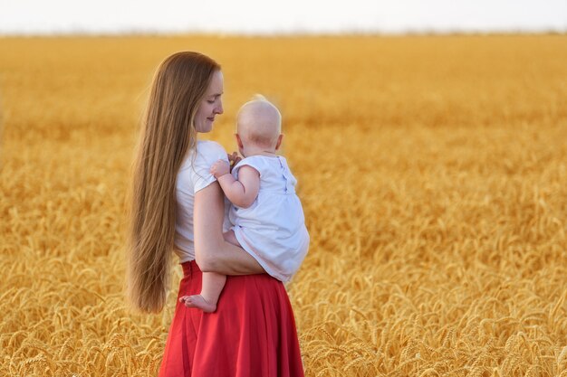 Nette junge Frau, die Baby im Hintergrundfeld des reifen Weizens hält. Mutter und Baby im Freien