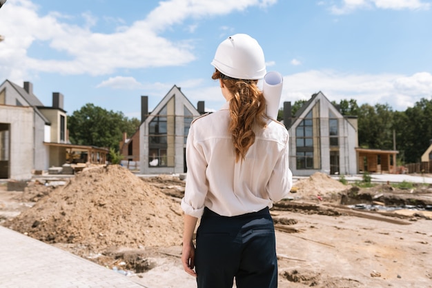 Nette junge Frau, die die Baustelle beim Halten einer Blaupause betrachtet