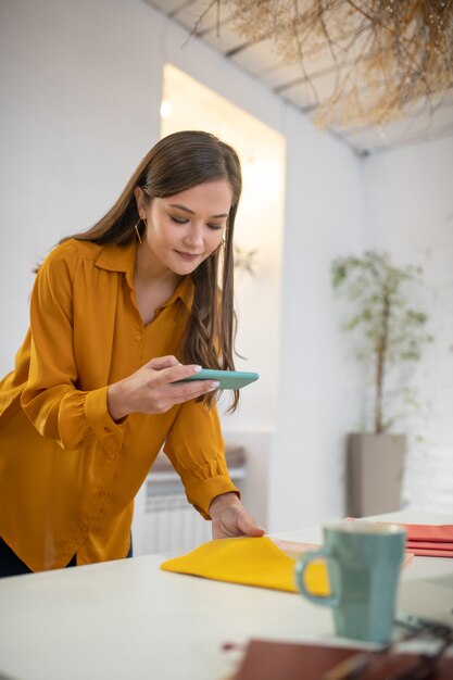 Nette junge Frau, die Fotos auf ihrem Smartphone macht, während sie bei der Arbeit beschäftigt ist