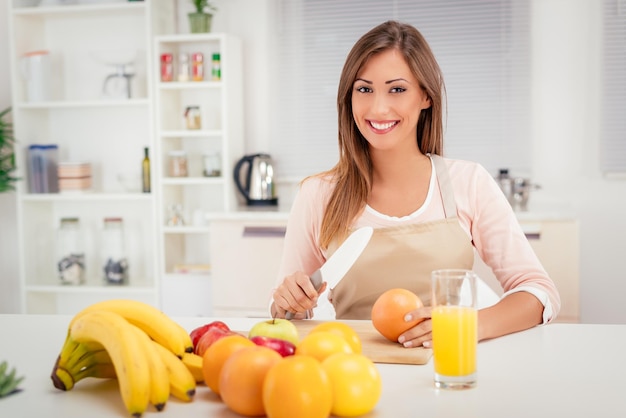 Nette junge Frau, die Grapefruit in der Küche schneidet. Blick in die Kamera.