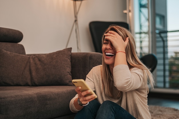 Nette junge Frau, die lustige Mitteilung am Telefon liest.