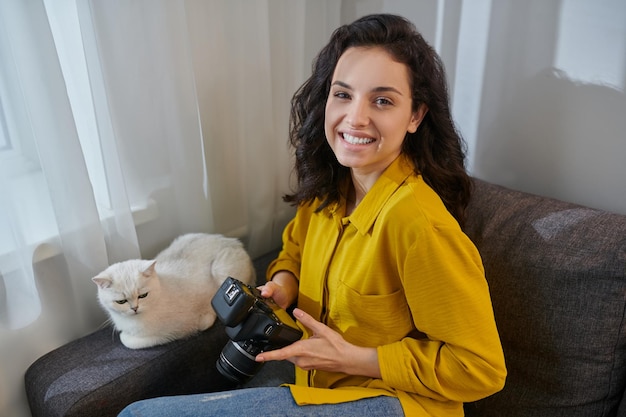 Nette junge Frau, die mit ihrer Katze neben ihr auf dem Sofa sitzt