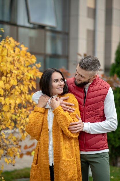 Nette junge Frau, die von ihrem Freund umarmt wird, während sie sich von ihm geliebt fühlt