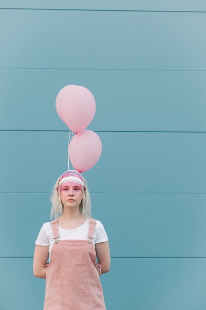 Nette junge Frau in den rosa Kleidern, die mit Luftballons stehen