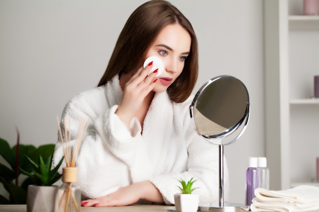 Nette junge Frau macht Make-up auf das Gesicht im Badezimmer