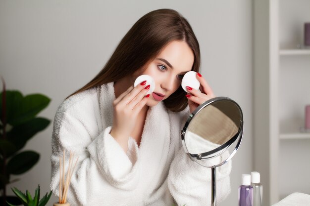 Nette junge Frau macht Make-up auf das Gesicht im Badezimmer