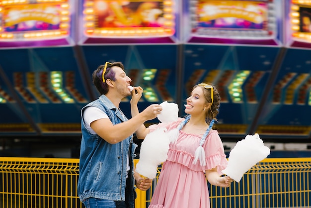 Nette junge Paare in der Liebe, die in einem Vergnügungspark stillsteht und Zuckerwatte sich einzieht. Liebestag, Valentinstag