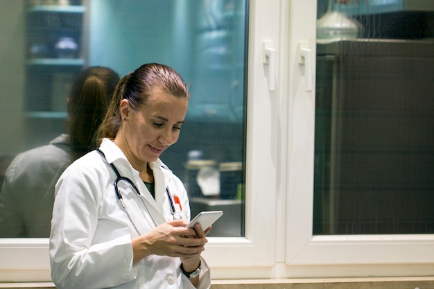 Nette junge Ärztin, die Smartphone steht und verwendet