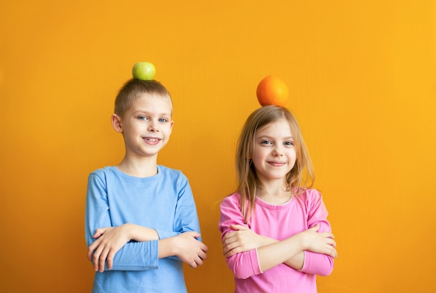 Nette Kinder an einer orangefarbenen Wand mit Obst spielen, setzen ihre Köpfe auf und lachen