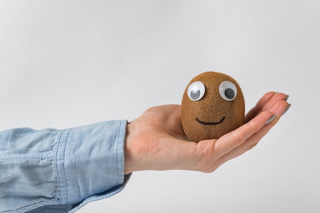 Nette Kiwi in der Handfläche auf weißem Hintergrund. Kiwi Charakter mit Googly Augen