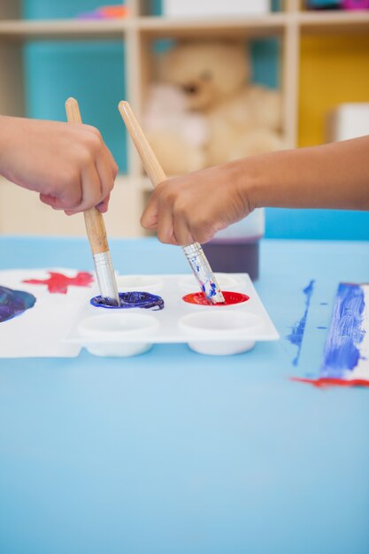 Nette kleine Jungen, die bei Tisch im Klassenzimmer malen