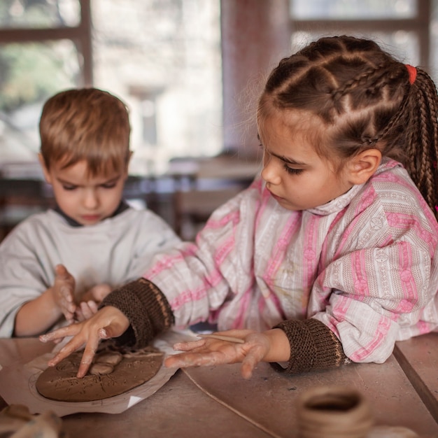 Nette kleine Kinder, die zusammen mit Modelliermasse in der Töpferwerkstatt, im Handwerk und in der Tonkunst spielen