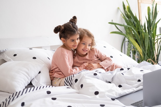 Nette kleine Kindermädchen im Pyjama mit Laptop im Bett zu Hause. Kinder, die Technologie verwenden.