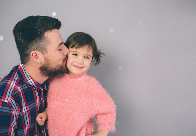 Nette kleine Tochter und ihr hübscher junger Vati spielen zusammen im Kinderzimmer. Vater und Kind verbringen Zeit miteinander, während sie im Schlafzimmer auf dem Boden sitzen.