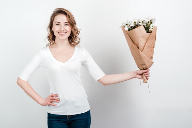 Nette kurzhaarige Frau im weißen leeren T-Shirt, das einen Blumenstrauß von bunten Blumen hält