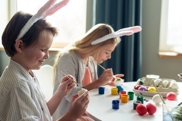 Nette, lächelnde Kinder malen sorgfältig Ostereier mit Farben