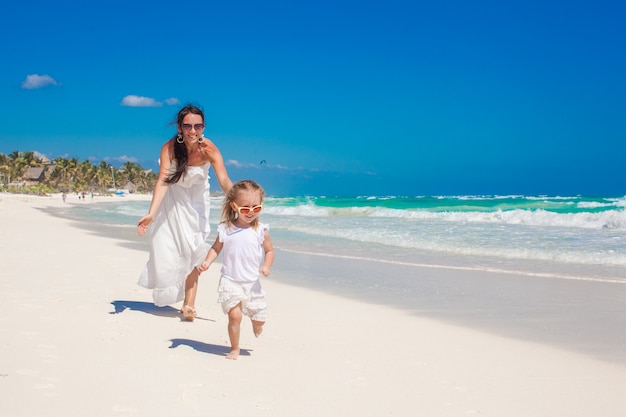 Nette lustige Tochter, die Spaß mit ihrer netten jungen Mutter auf dem weißen sandigen Strand in Mexiko hat
