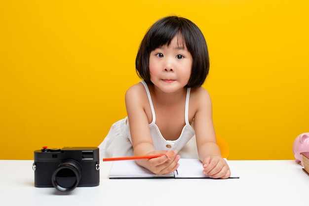 Nette Mädchenbilder Asien schreibt ein Buch Im Büro für fleißige Kinder Intelligente Kinder Weißer Tisch auf gelbem Hintergrund