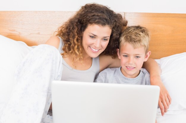 Nette Mutter und Sohn, die auf Bett unter Verwendung des Laptops sitzt