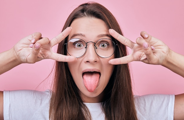 Nette nette Frau zeigt die Finger des Friedens ihre Zunge heraus haftend