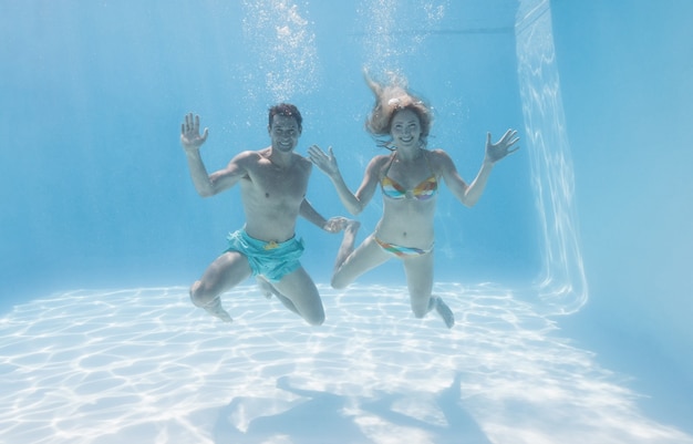 Nette Paare, die an der Kamera Unterwasser im Swimmingpool lächeln