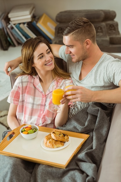 Nette Paare, die auf Couch mit Frühstück sich entspannen