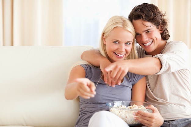 Nette Paare, die Fernsehen beim Essen des Popcorns aufpassen