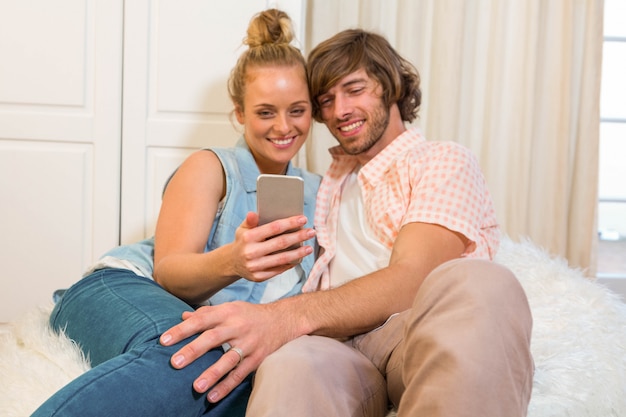 Nette Paare, die Smartphoneschirm im Wohnzimmer betrachten