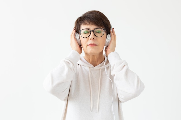 Nette positive Frau mittleren Alters in Pullover und Brille hört Musik mit Drahtkopfhörern