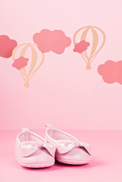 Nette rosa Schuhe des Babys über dem rosa Pastellhintergrund mit Wolken und Ballons