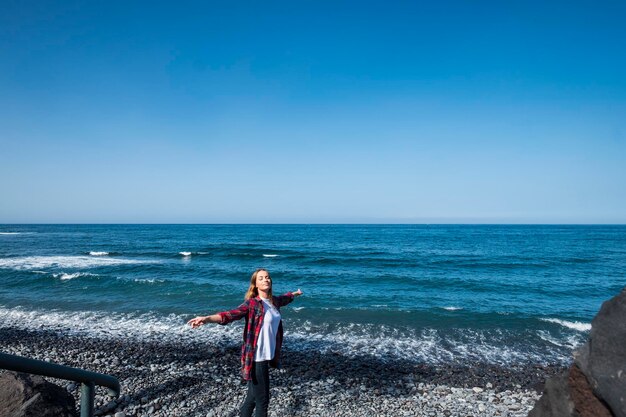 Nette schöne junge kaukasische frau genießen und haben spaß am strand im sommerferienferienkonzept für weibliche reisende in trendigen hipster-kleidungsozean im hintergrund