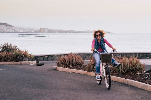 Nette schöne junge kaukasische Frau mit lockigem Haar im Wind bewegte sich mit einem Fahrrad und hat Spaß