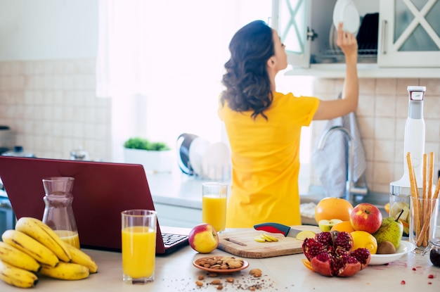 Nette schöne und glückliche junge brünette Frau in der Küche zu Hause bereitet Obstsalat vor