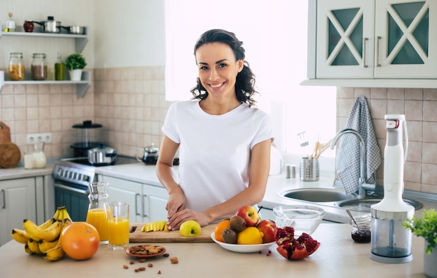 Nette schöne und glückliche junge brünette Frau in der Küche zu Hause hackt Früchte