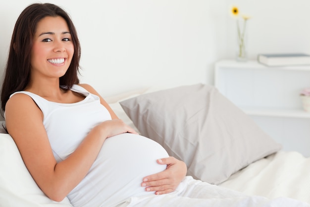 Nette schwangere Frau, die ihren Bauch beim Lügen auf einem Bett berührt