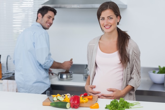 Nette schwangere Frau, die ihren Bauch in der Küche hält