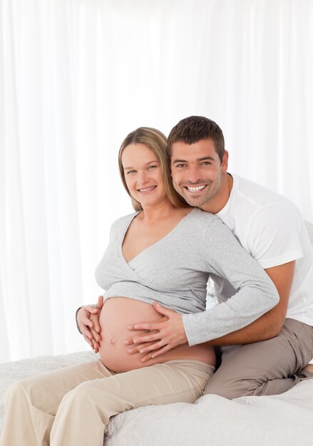 Nette schwangere Frau, die ihren Bauch mit ihrem Ehemann im Schlafzimmer berührt