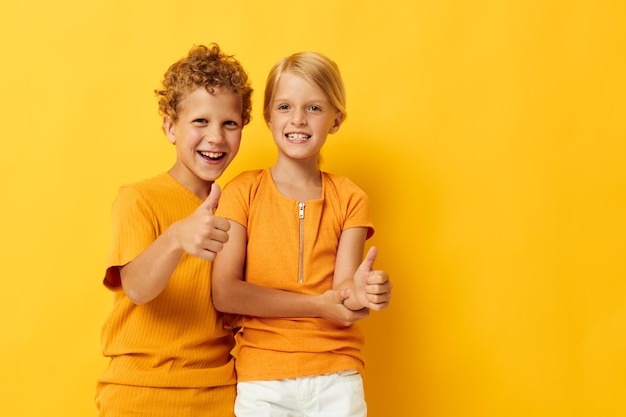 Foto nette stylische kinder in gelben t-shirts, die seite an seite stehen, kindheitsgefühle, isolierter hintergrund, un...