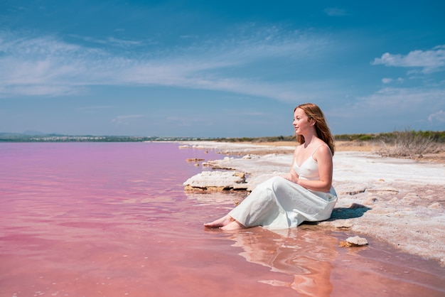 Nette Teenagerfrau, die weißes Kleid trägt, das auf einem erstaunlichen rosa See sitzt