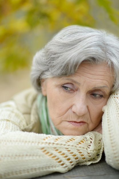 Nette traurige alte Frau auf dem Herbsthintergrund