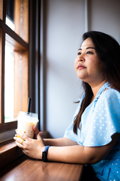 Nette übergewichtige Frau im Kaffeecafé, glückliche asiatische Frau in einem Café mit Plastikbecherkaffee