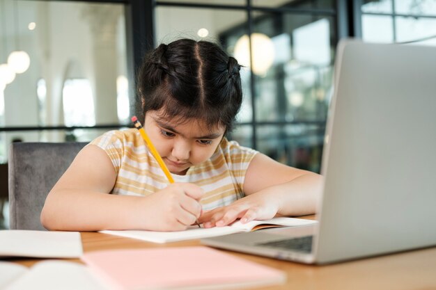 Nette und glückliche kleine Mädchen, die Laptop-Computer verwenden und über ein Online-E-Learning-System lernen.