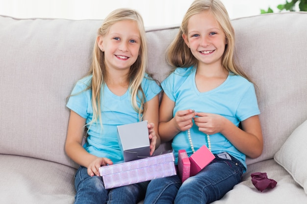 Nette Zwillinge, die das Geburtstagsgeschenk auspackt, das auf einer Couch sitzt