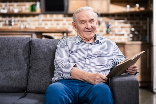 Netter älterer Mann, der lächelt, während er ein Buch zu Hause liest