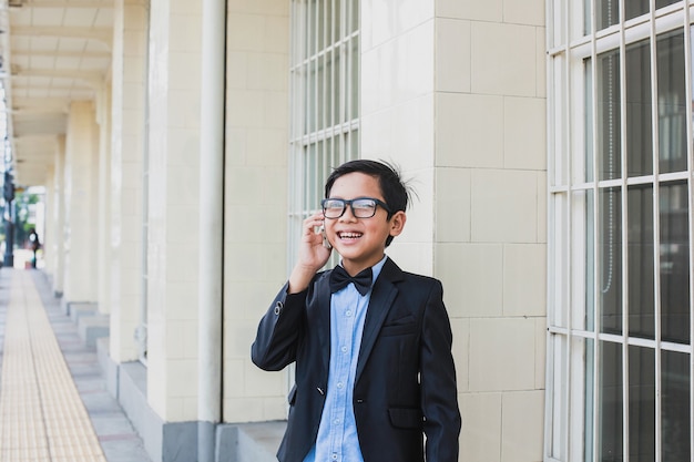 Netter asiatischer Junge, der Vintage schwarzen Anzug und Brille spricht, spricht am Telefon beim Lächeln